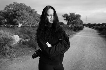 bellissima ragazza mora vestita di nero guarda seria con una macchina fotografica a tracolla