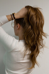 Fototapeta premium Caucasian woman holding her hair on top of her hair, posing from the side, model wears golden glasses , watch on her hand and white blouse