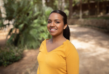 Portrait of happy brazilian lady standing outdoors, looking and smiling at camera, walking in park