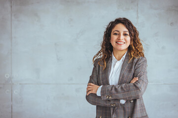 Fototapeta na wymiar Confident young woman standing with folded arms on gray wall. Portrait of smiling businesswoman with arms crossed isolated against grey background with copy space.