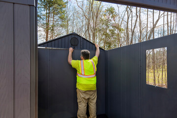 There is worker assembling plastic vinyl storage shed for backyard near house