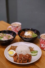 Portrait or vertical shot of a set of Malaysian cuisine containing Steamed Chicken Rice, Nasi Lemak, Chili Pan Mee, and two mugs of Thai Tea on a wooden table with blurred background
