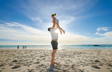 Father lifting daughter, having fun on the beach. A smiling young man playing with his cute little...
