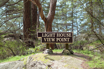 Lighthouse view point signage in park in front of tall tree foliage. Large wooden sign for park...