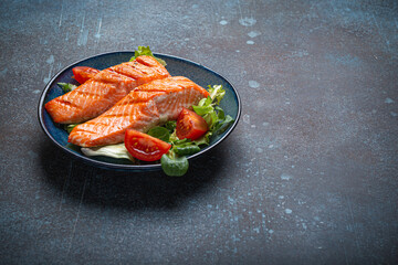 Grilled fish salmon steak with vegetables salad on ceramic plate on rustic stone background angle view, balanced diet or healthy nutrition salad meal with salmon and veggies, space for text