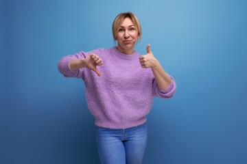 portrait of charming pleasant blond young woman in purple sweater with grimace showing like and...