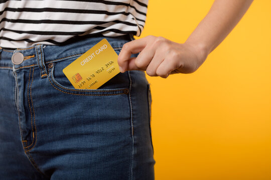 hand of person woman holding plastic credit card out of the pocket blue jean plants isolated on yellow studio background. online shopping payment, bill, currency, pay money, finance concept.