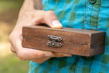 Man holding a simple small closed classy stylish wooden box, container. Gift, present, important items storage, carrying case abstract concept, object detail, closeup, one person. Secret box, closed