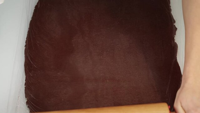 Baker rolls chocolate dough sheet covered with foil on table