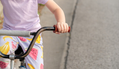 Fototapeta na wymiar Young anonymous unrecognizable school age child riding an old used second hand bike, holding hands on handlebars closeup, detail, one person, blurred background, copy space. Old bicycle, cycling