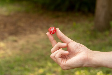 Anonymous man holding up one single simple red 20 sided RPG game dice, object held in hand detail,...