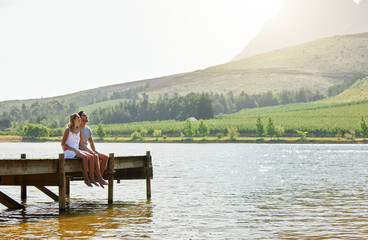 We can sit and admire this view all day long. Shot of a loving couple sitting on a jetty at a lake.