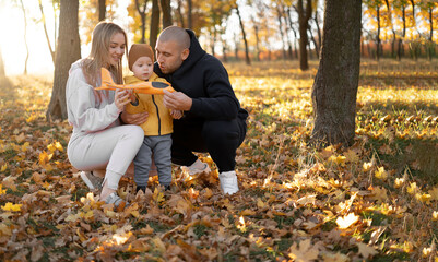 Happy family, mother, father and kid playing with toy plane are walking in park at sunset.