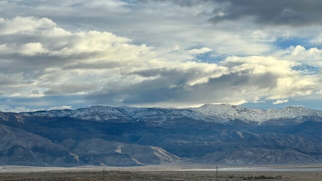 Wide view of snow-capped mountains, with dramatic clouds overhead, seen from freeway near Lone Pine, California