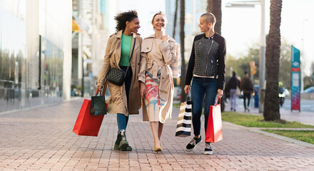 Three happy women friends with shopping bags walking on street in the city for Spring sales