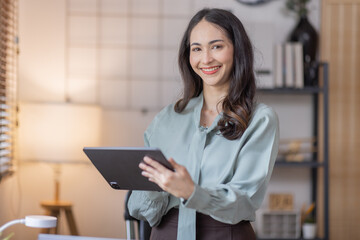 Young business Asian woman using tablet , standing near the window in workplace
