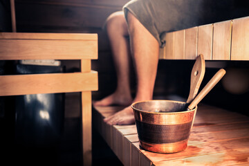 Sauna and man in Finland. Wood spa steam room. Finnish summer cabin home or hotel. Person with towel. Hot and healthy therapy for people. Water bucket. Relax and lifestyle. Traditional heat treatment.