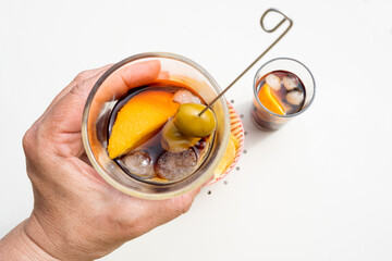 hand holding a glass of vermouth, in the background an aperitif bowl, the viewpoint of the person...