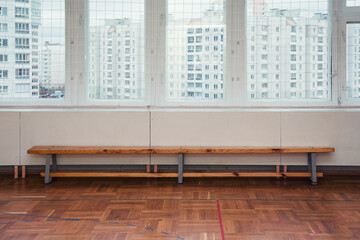 Wooden sport bench stands on empty floor against big window indoor of school gym. Sport training concept.
