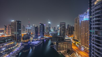 Aerial view to Dubai marina skyscrapers around canal with floating boats all night timelapse
