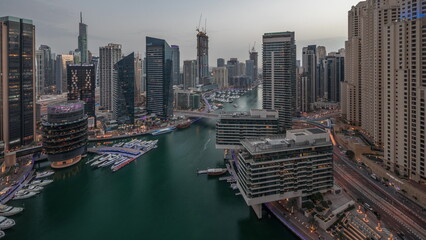 Aerial view to Dubai marina skyscrapers around canal with floating boats day to night timelapse