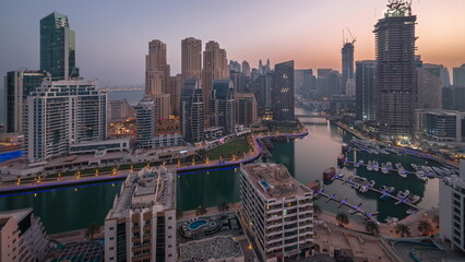 Obraz premium Dubai Marina with several boats and yachts parked in harbor and skyscrapers around canal aerial night to day timelapse.