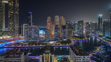 Panorama showing Dubai Marina with several boat and yachts parked in harbor and skyscrapers around canal aerial night timelapse.