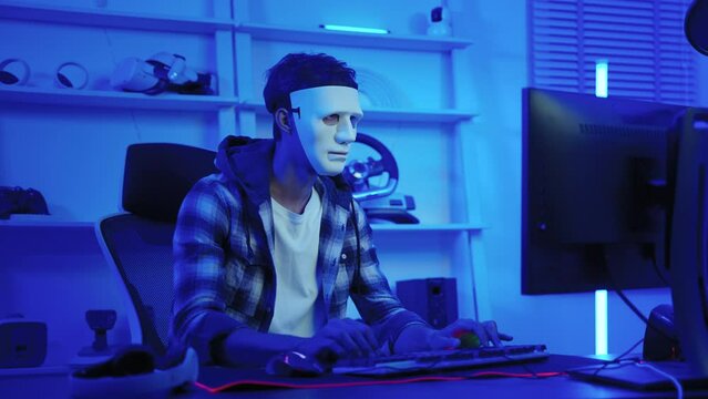 hacker wearing a white mask is using a computer to steal confidential information.Concepts: computer crime, burglary, business security on computer networks
