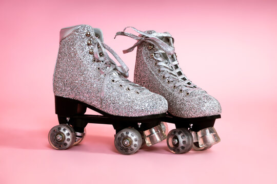 Pair of glitter silver stylish roller skates on pink background.