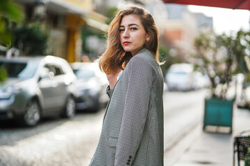 Fototapeta premium A beautiful young girl in a gray jacket is standing on a city street.
