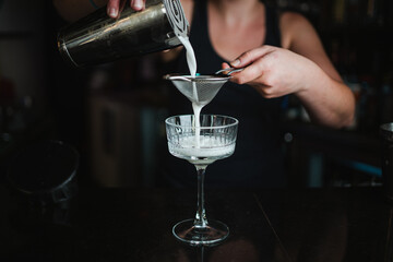 Shot of a woman bartender straining a cocktail from the shaker into the glass
