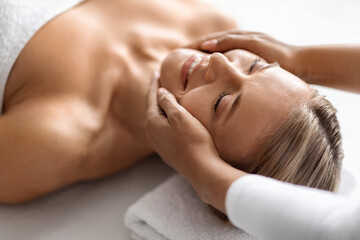 Fototapeta na wymiar Beautiful middle aged woman enjoying face lifting massage in spa salon