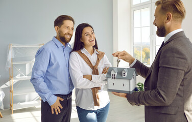 Realtor handing over house keys to happy buyers. Professional real estate agent with toy house...