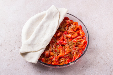 Glass form with red bell peppers, onions and spices half covered with puff pastry on a beige textured background, top view. Cooking stage of delicious red pepper pie