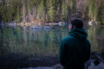 jeune homme se tenant debout au bord d'un lac de montagne. Il admire le paysage magnifique.