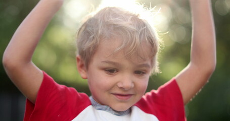 Happy child boy celebrating raising arms. Portrait of blond toddler infant boy feeling joy cheerful