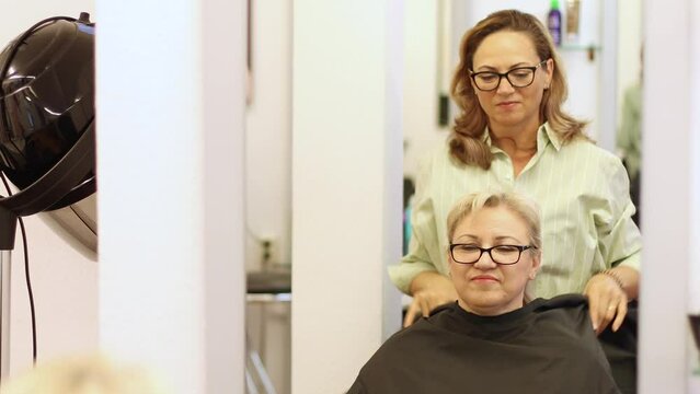 hairdresser woman in glasses covers client of salon client woman with glasses
