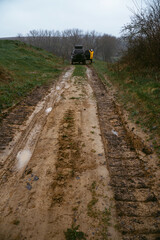 Country road, selective focus. clay and stones, mud and puddles. A woman in a yellow jacket with off-road vehicle. Cold spring day, landscape. A car for tourism and extreme adventures. Vertical photo