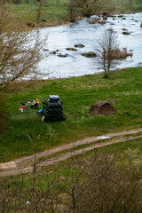 Distance view. Copy space. Morning landscape with a tents and off road vehicle, the river bank and rocks in the background. Spring camping. Tourism and vacation. Vertical photo.