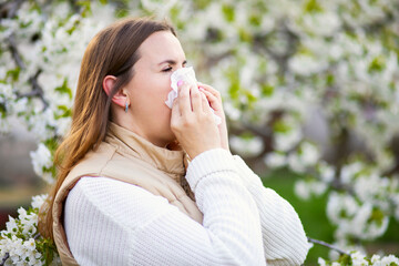 Sneezing woman with a nose wiper among the flowering trees in the park