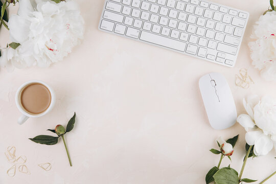 Feminine workspace with cup of coffee milk, keyboard, stylish office writing supplies and on a pastel teble