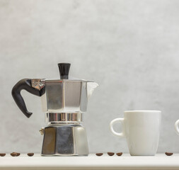 Metal geyser coffee maker on table with cup