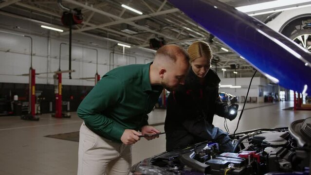 A spare parts selection manager together with a female car mechanic during car diagnostics. Against the background of a modern car repair line