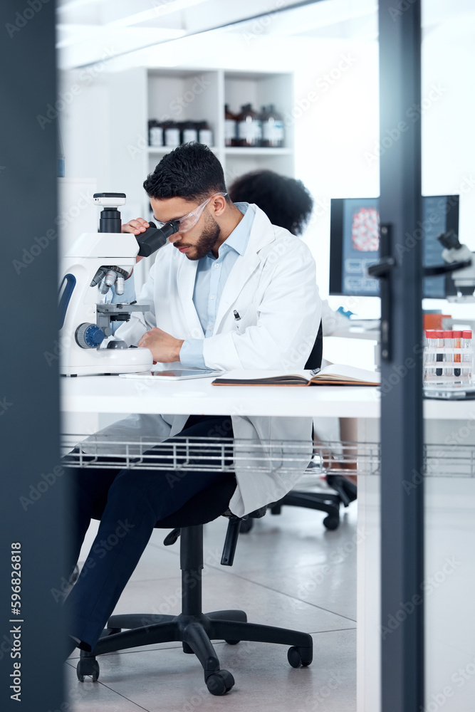 Aufkleber One mixed race scientist wearing safety goggles while analysing medical test samples with a microscope in a lab. Young indian man investigating with forensic research and experiments to develop a cure