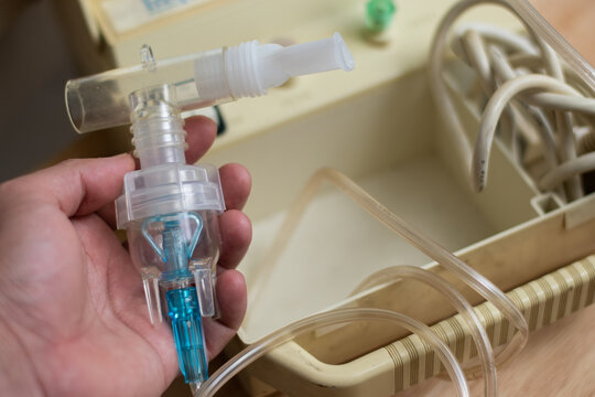 Hand holding a nebulizer steam tube with the vaporizer in the background with copy space