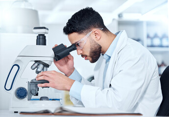 Naklejka na ściany i meble One serious young male medical scientist sitting at a desk and using a microscope to examine and analyse test samples on slides in a hospital. Hispanic healthcare biochemist professional discovering