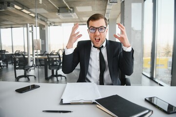 Angry businessman sitting at the table and screaming.