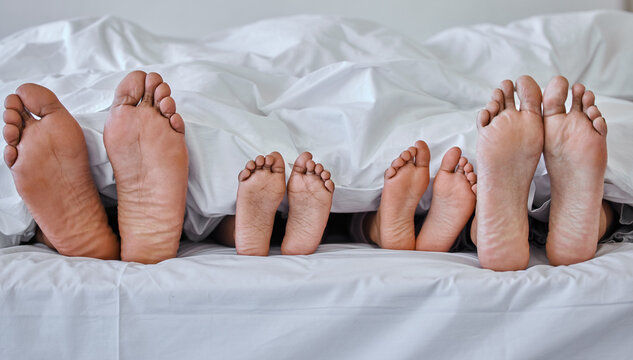 Being a family means you are a part of something. Shot of a family laying barefoot on a bed at home.