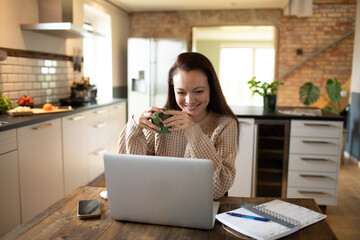 Young adult woman using a laptop in a kitchen