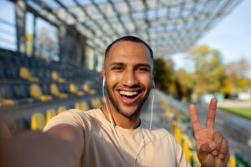 Close-up photo. Young african american male sportsman standing in headphones at stadium and taking...